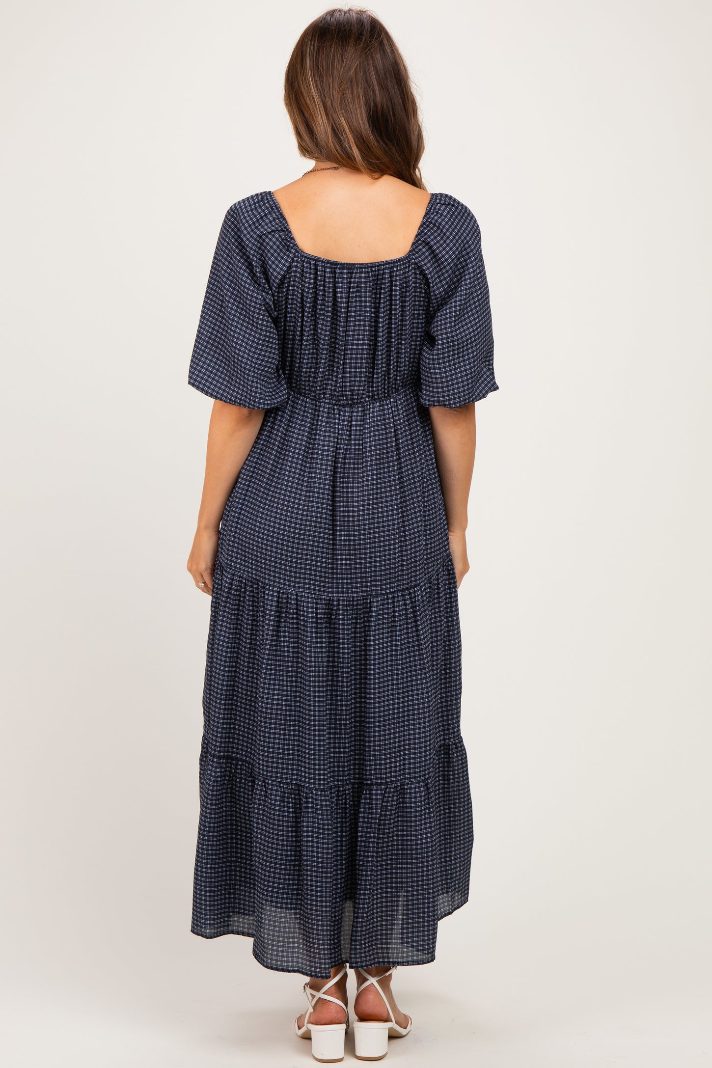 woman wearing a navy blue maternity maxi dress with short puff sleeves and tiered ruffles, showing the back view