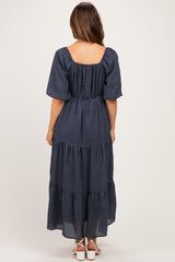 woman wearing a navy blue maternity maxi dress with short puff sleeves and tiered ruffles, showing the back view