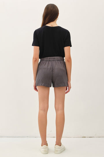 woman wearing a black t-shirt and gray shorts, viewed from the back, standing against a plain background
