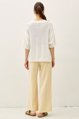 woman wearing a loose white knit sweater and wide leg beige pants, viewed from the back