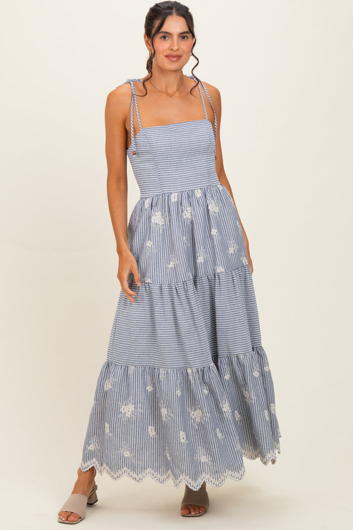 woman wearing a blue and white striped maxi dress with embroidered flowers and a tiered skirt