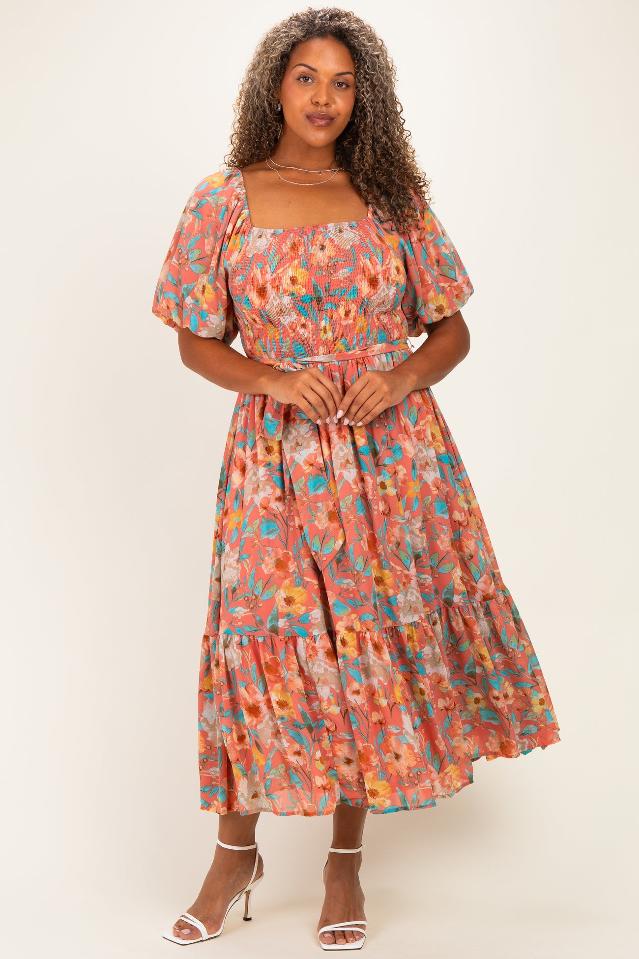 woman wearing a floral plus-size midi dress with puff sleeves and a tiered skirt, posed with hands on waist