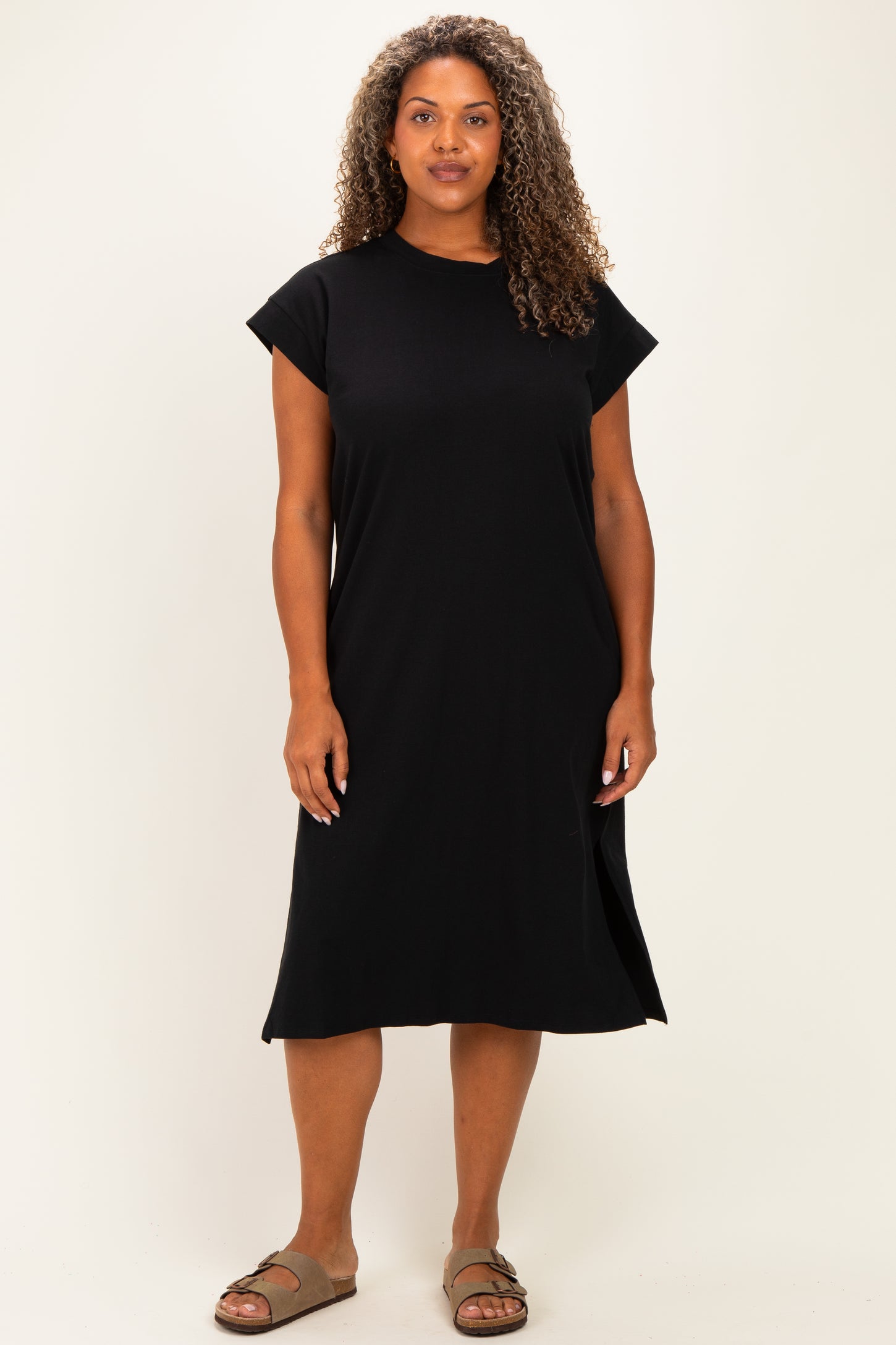 woman wearing a relaxed black short sleeve plus size dress with side slits and standing against a neutral background
