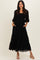 woman wearing a black lace maxi dress with smocked bodice and puff sleeves, standing with pockets visible