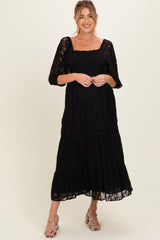 woman wearing a black lace maternity maxi dress with three-quarter sleeves and a smocked bodice, holding her baby bump