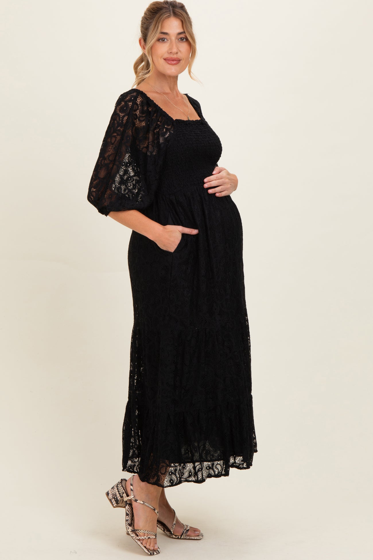 woman wearing a black lace maternity dress with puff sleeves and pockets, cradling her baby bump