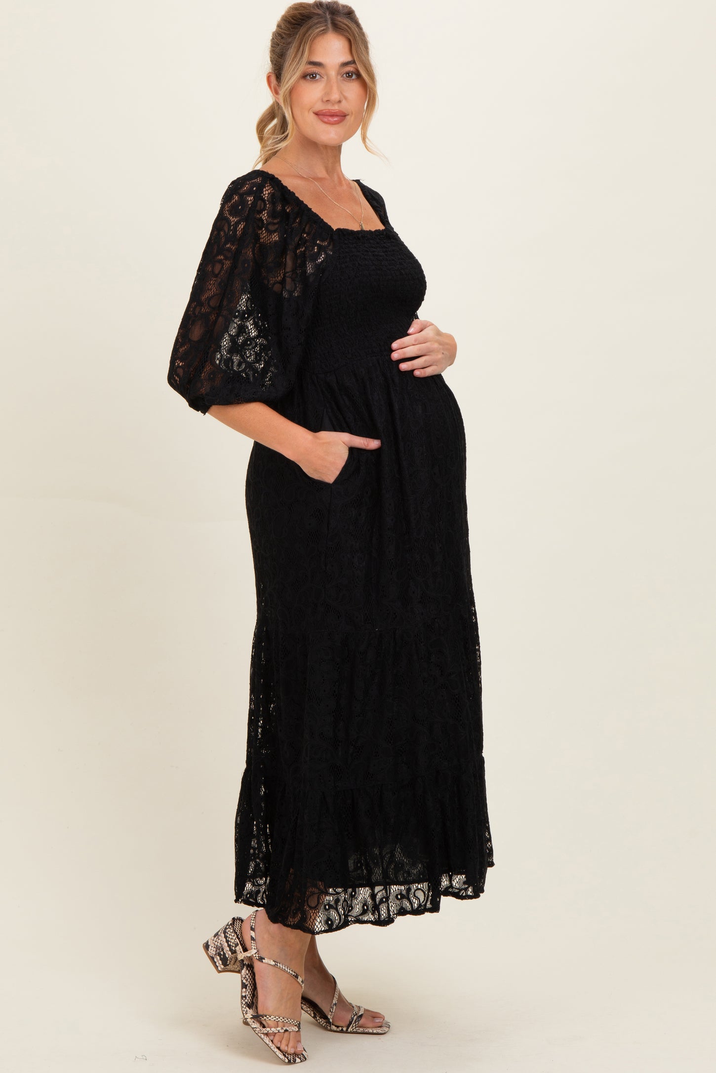 woman wearing a black lace maternity dress with puff sleeves and pockets, cradling her baby bump