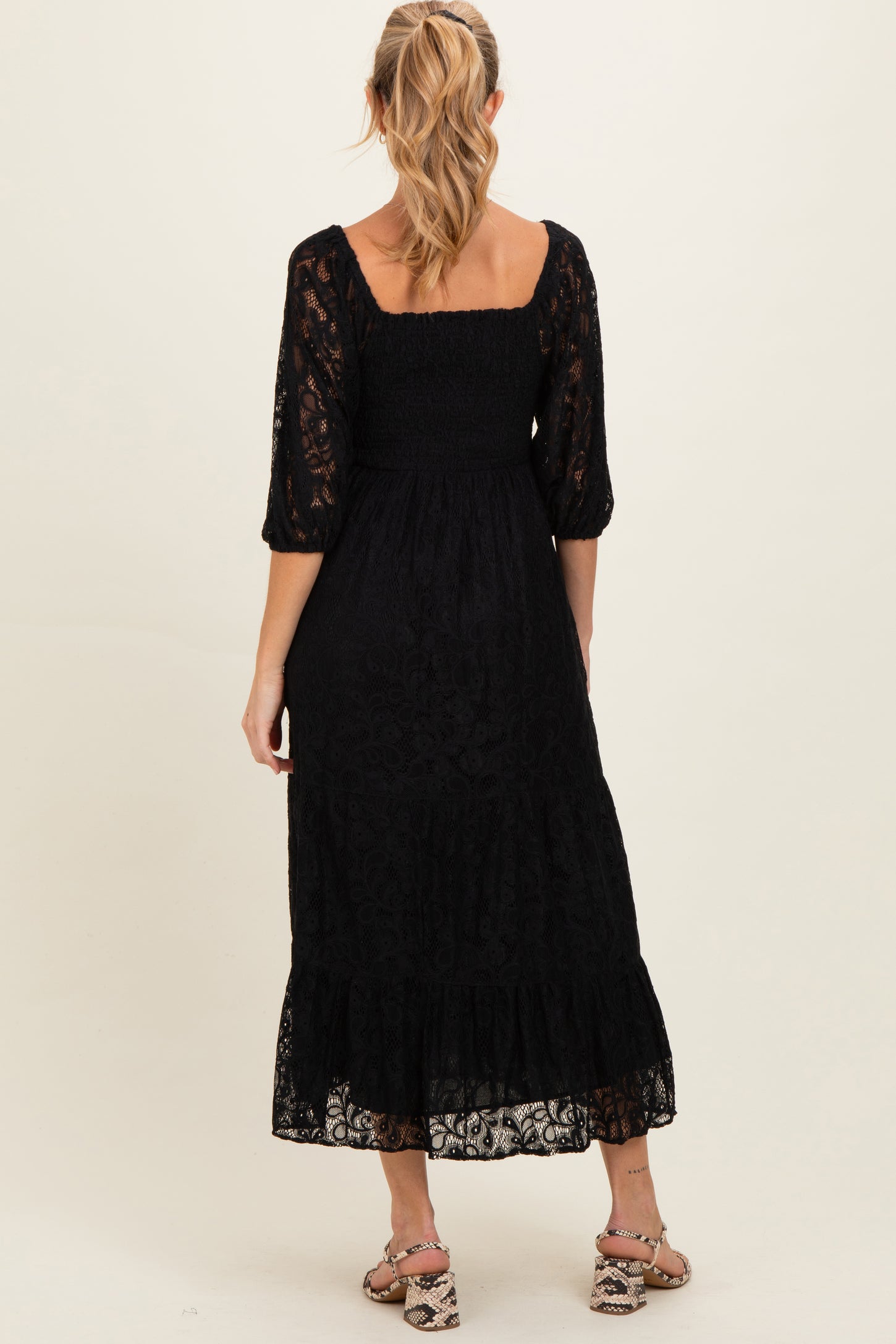 woman wearing a black lace maternity dress with a smocked bodice and three-quarter sleeves, showing a flowing skirt