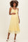 woman wearing a yellow lace maternity dress with spaghetti straps and a flowy hem, gently cradling her baby bump