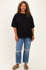 woman wearing a black oversized t-shirt and distressed blue jeans, standing against a neutral background