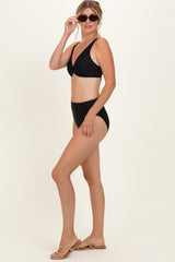 woman wearing a black two-piece bikini with a twisted top and high-waisted bottom, accessorized with sunglasses