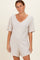 woman wearing a beige short sleeve maternity romper with a v-neck and two pockets, highlighting her baby bump