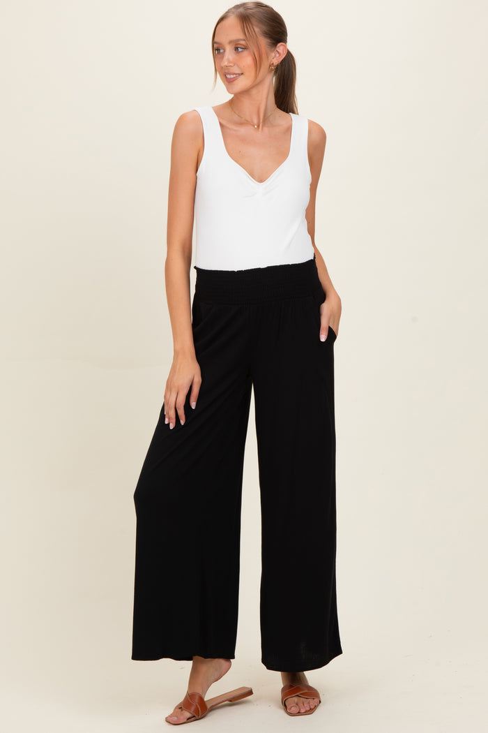 woman wearing a white sleeveless maternity top and black wide-leg maternity pants with pockets