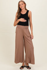woman wearing a black ribbed tank top and brown maternity wide-leg pants, holding her baby bump