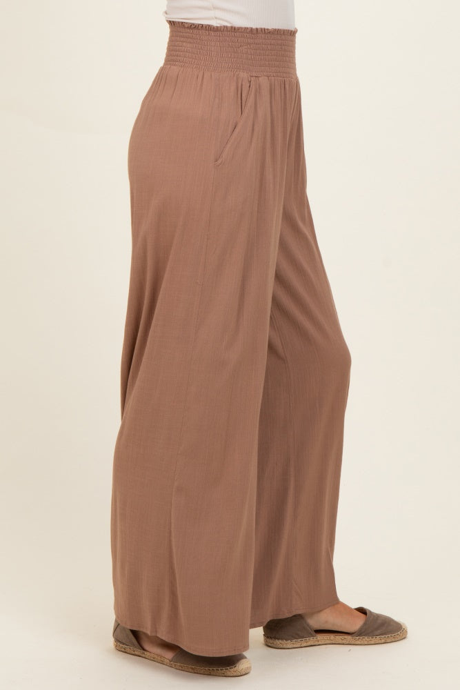 woman wearing a taupe wide-leg pant with a smocked waist and side pockets, styled with flat shoes