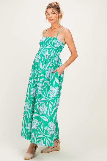 woman wearing a green floral maternity maxi dress with a smocked bodice and pockets, holding her baby bump