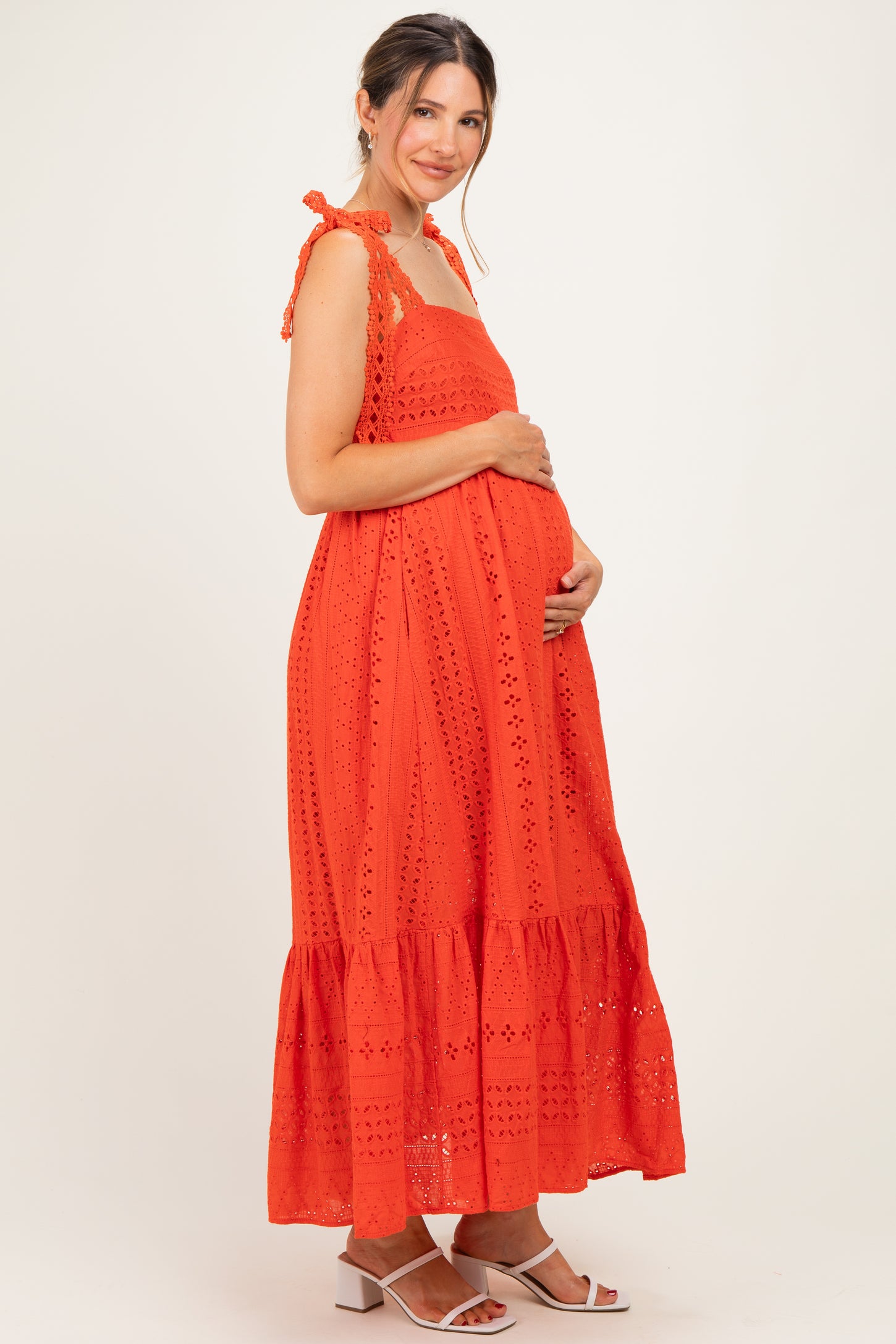 woman wearing an orange maternity dress with eyelet details and a ruffle hem, gently cradling her baby bump