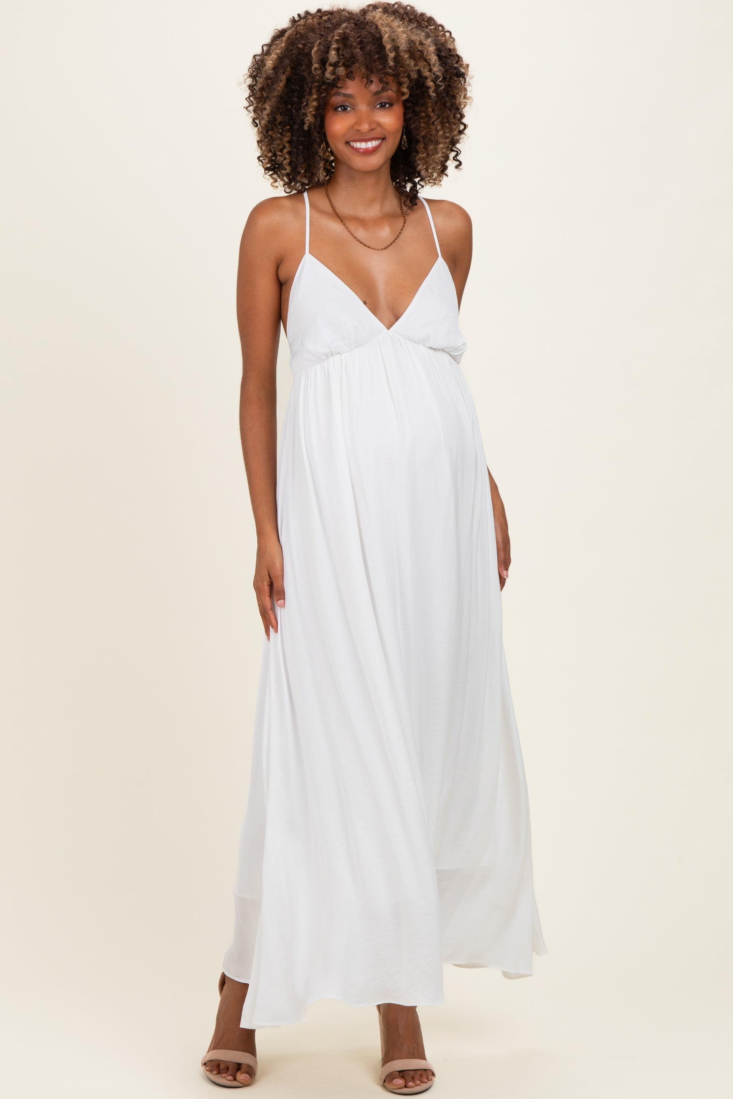 woman wearing a white maternity maxi dress with a deep v-neck and adjustable straps, showcasing her baby bump