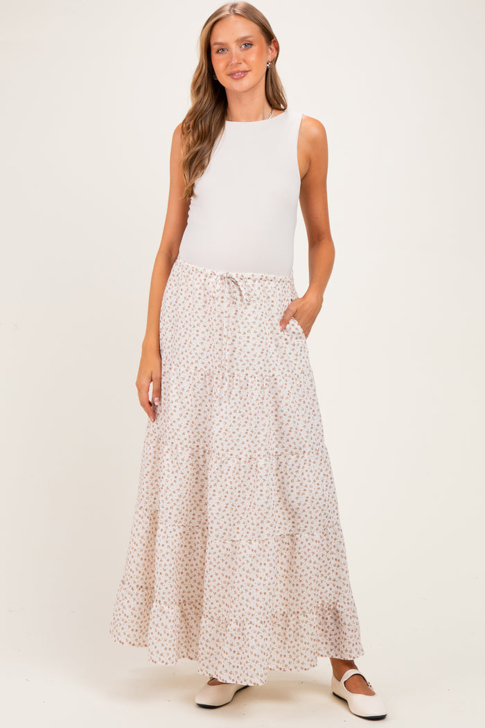woman wearing a white sleeveless top and a floral printed maxi skirt with pockets, styled for maternity wear