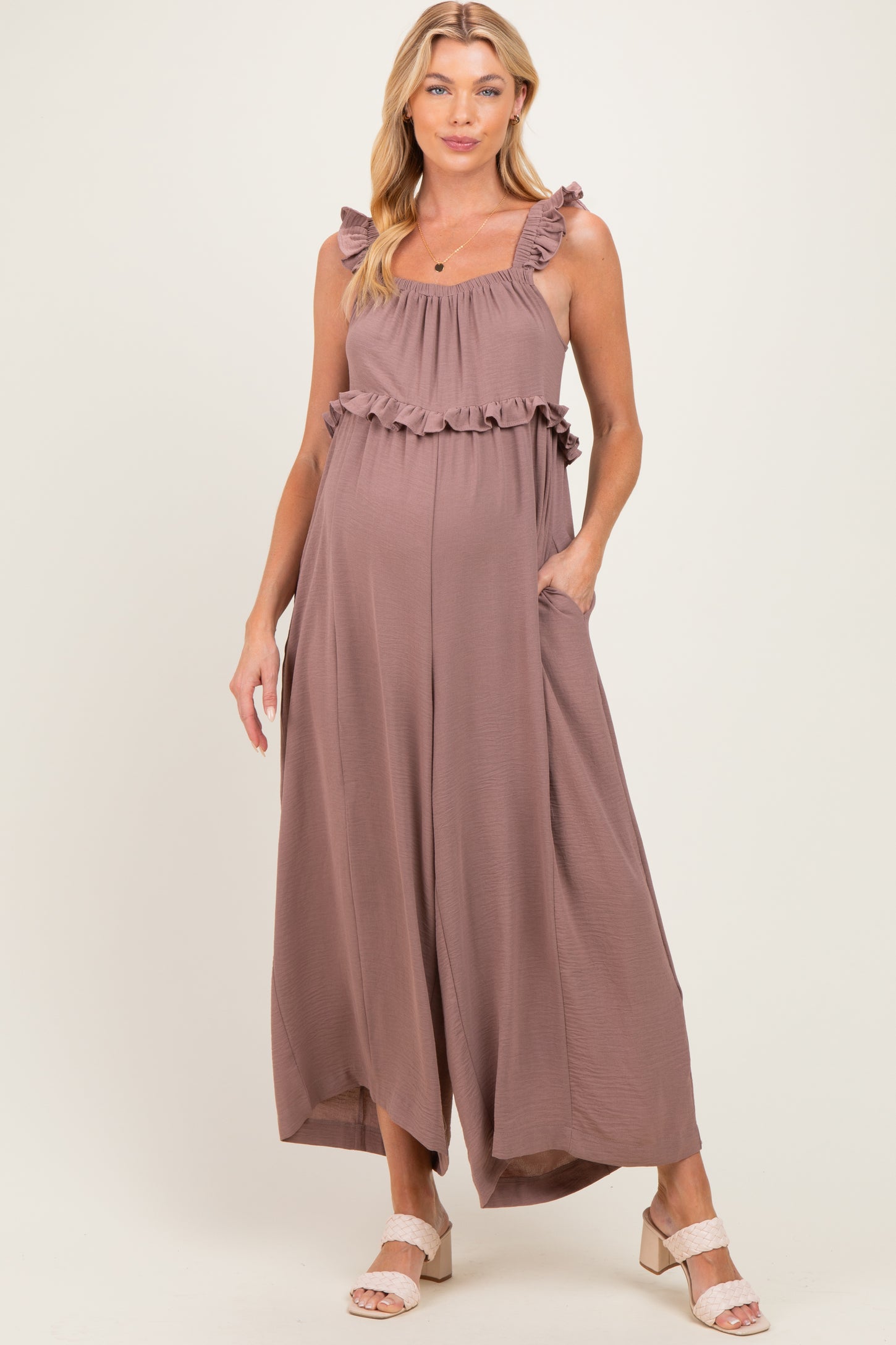 woman wearing a mauve maternity jumpsuit with ruffled straps and pockets, showing her baby bump