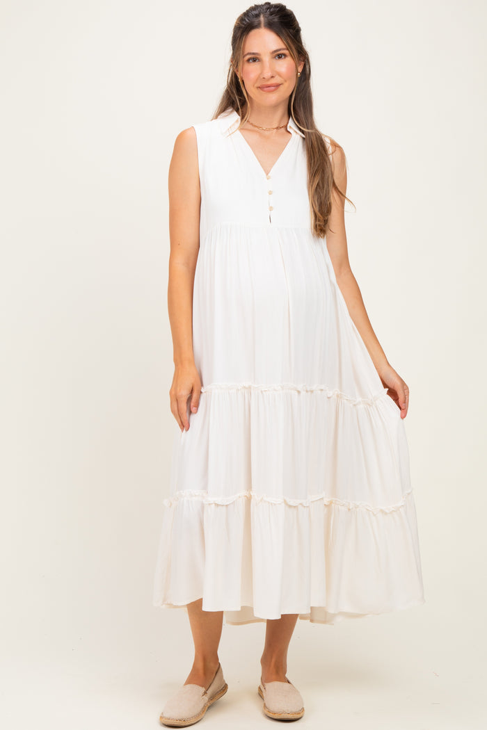 woman wearing a white sleeveless maternity dress with a button closure and tiered ruffle hem, showing her baby bump