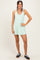 woman wearing a light green sleeveless casual dress with side pockets and black athletic shoes