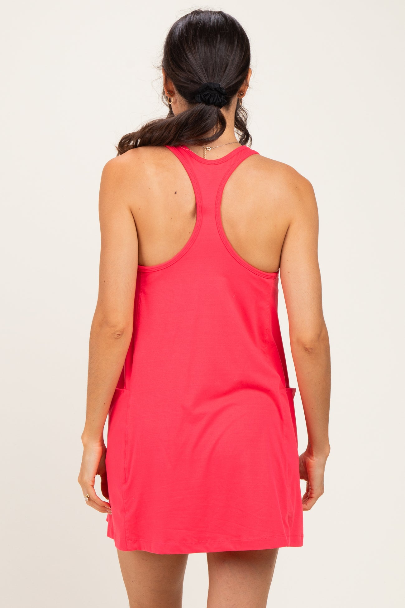 woman wearing a coral pink sleeveless dress with a relaxed fit and side pockets, viewed from the back