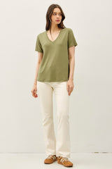woman wearing a green short sleeve v-neck t-shirt and white flared jeans with brown sneakers