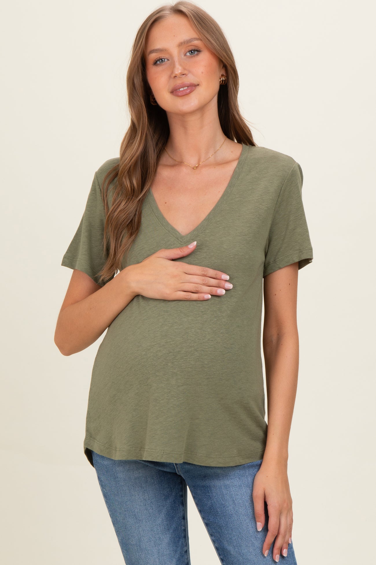 woman wearing an olive green short sleeve maternity top and holding her baby bump