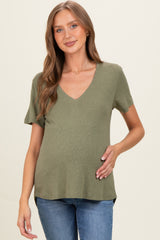 woman wearing an olive green short sleeve maternity top and holding her baby bump