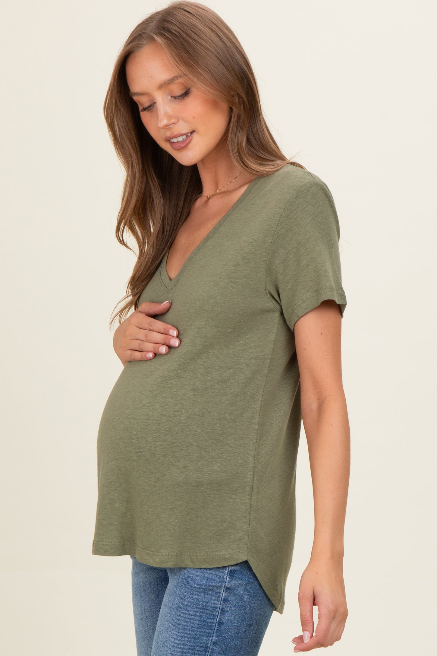 woman wearing an olive green v-neck maternity top and holding her baby bump