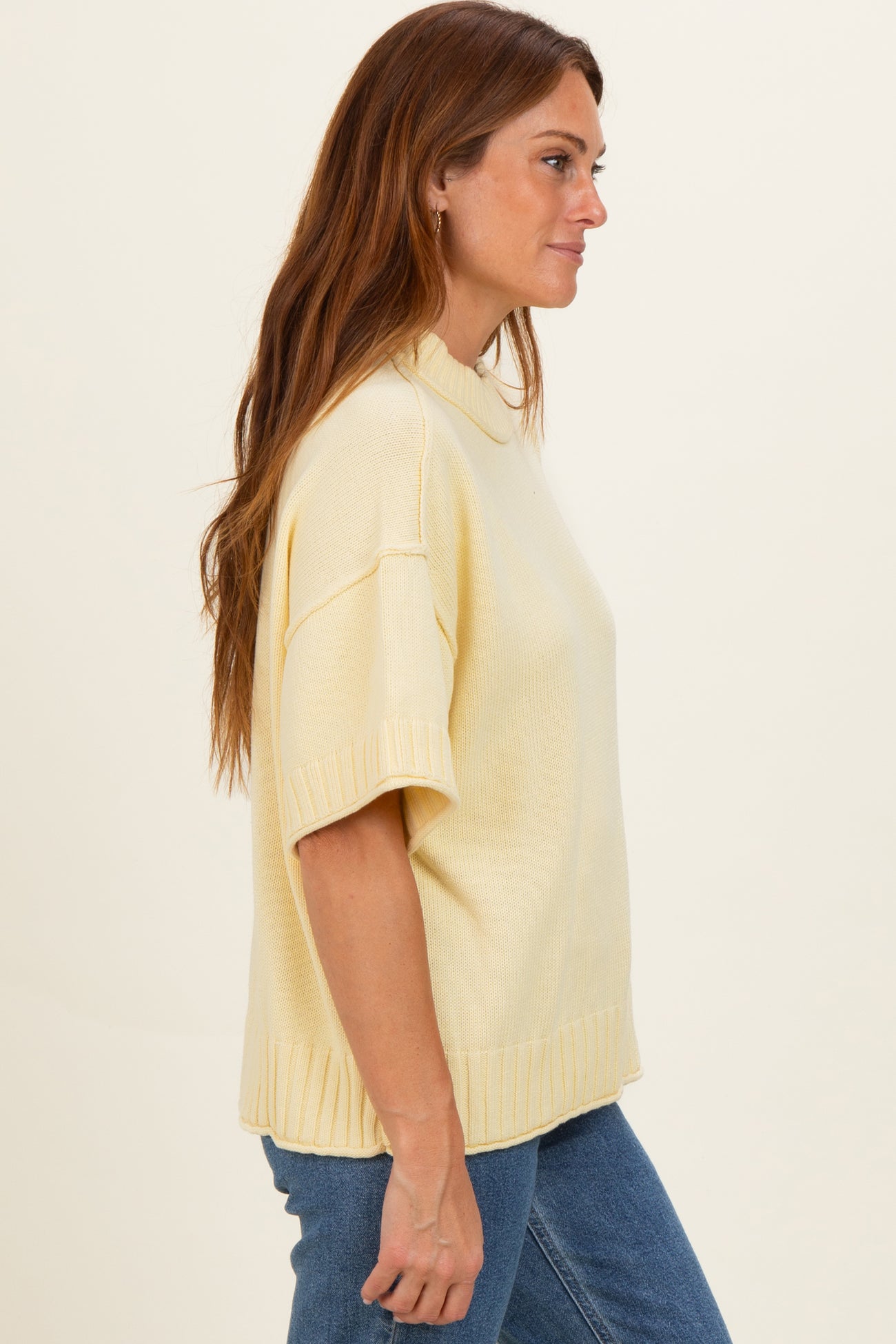 woman wearing a light yellow short sleeve casual sweater with a relaxed fit and ribbed hem, styled with blue jeans