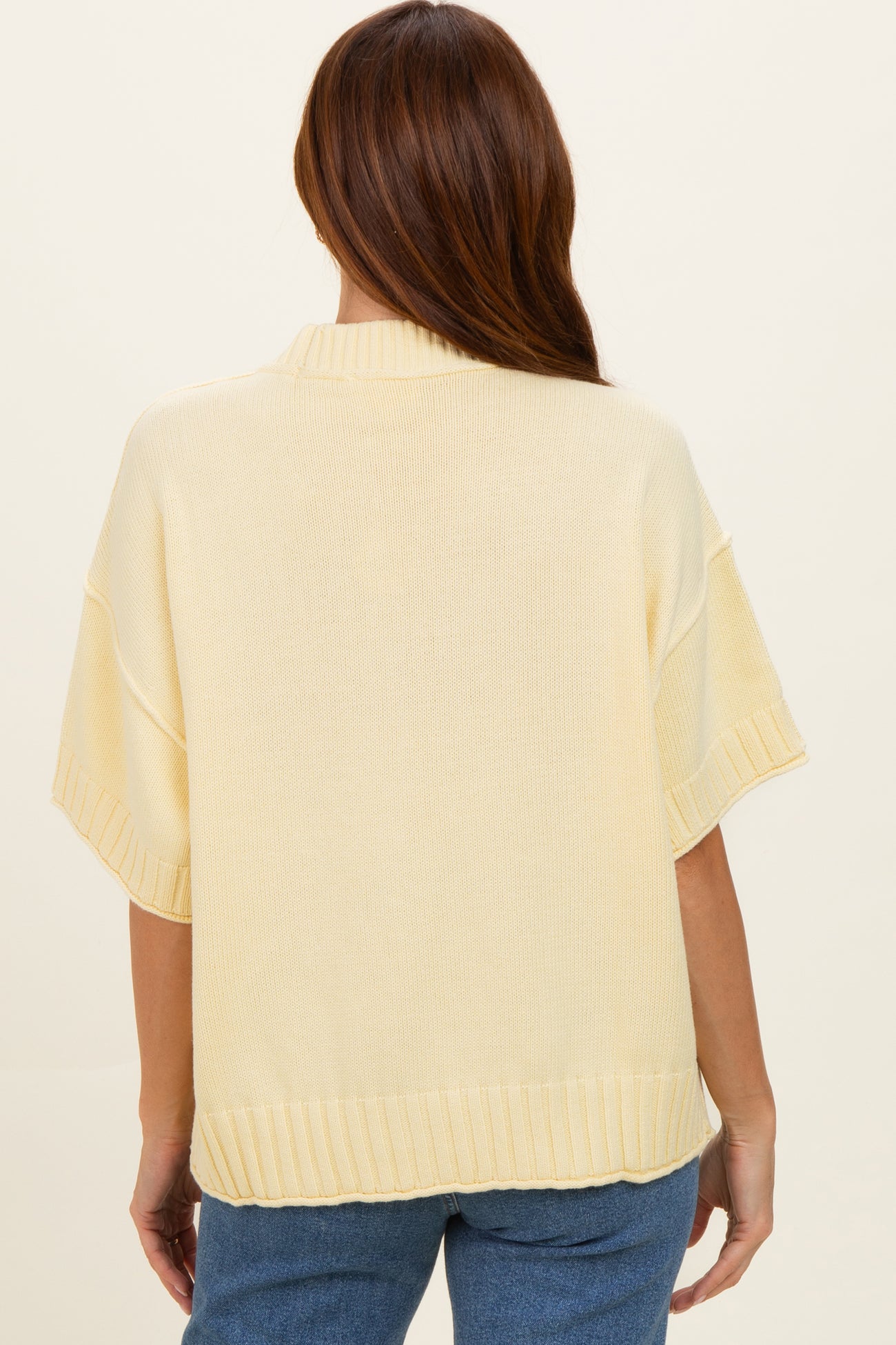woman wearing a light yellow oversized sweater with ribbed hem and short sleeves, viewed from the back