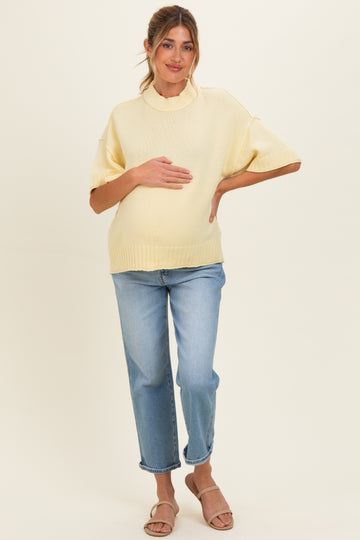 woman wearing a light yellow maternity sweater and blue jeans while holding her baby bump