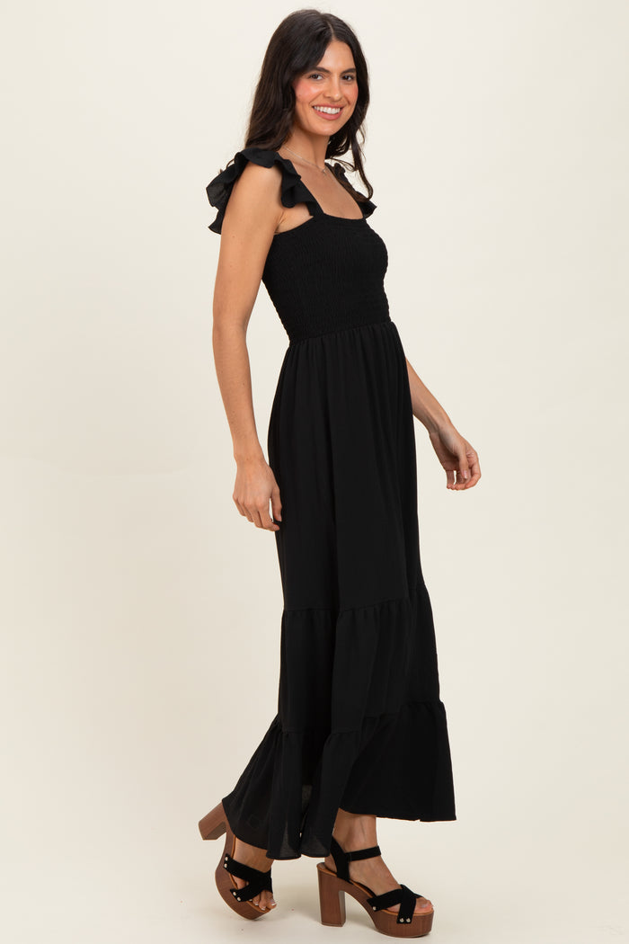 woman wearing a black maxi dress with ruffled straps and a tiered skirt, paired with platform heels