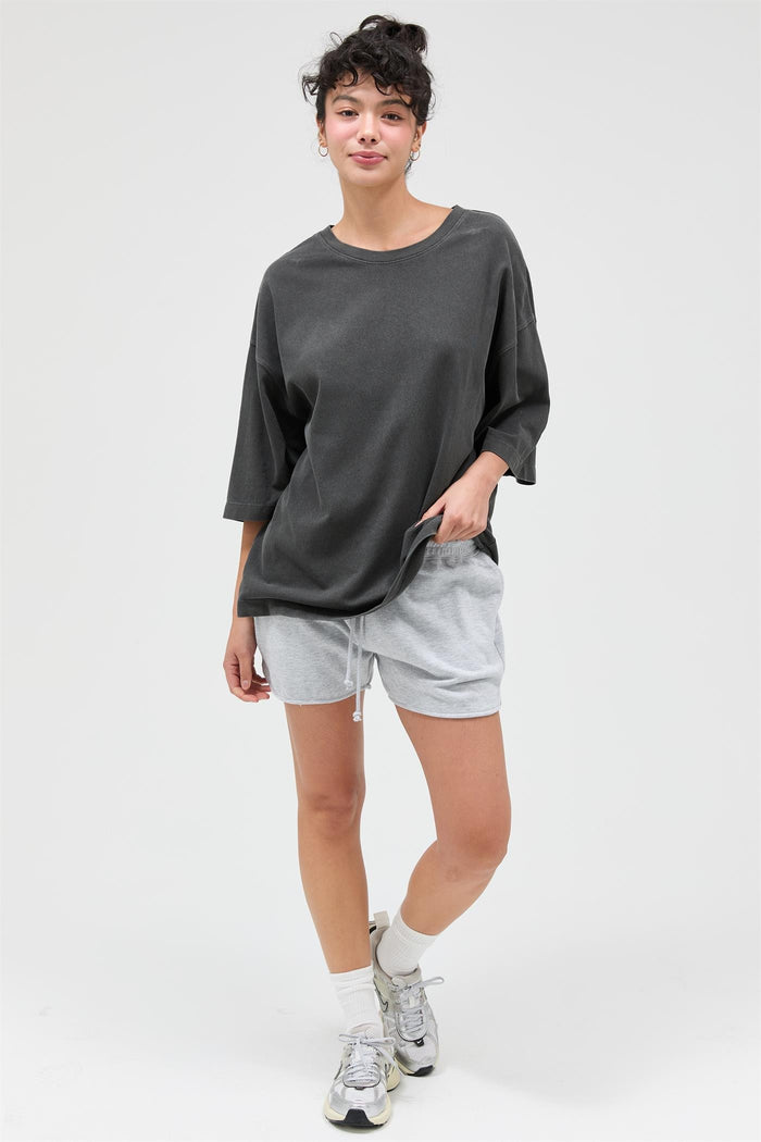 woman wearing an oversized dark gray t-shirt and light gray shorts, standing with one hand in her pocket