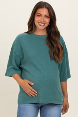 woman wearing a teal maternity top with short sleeves and holding her baby bump