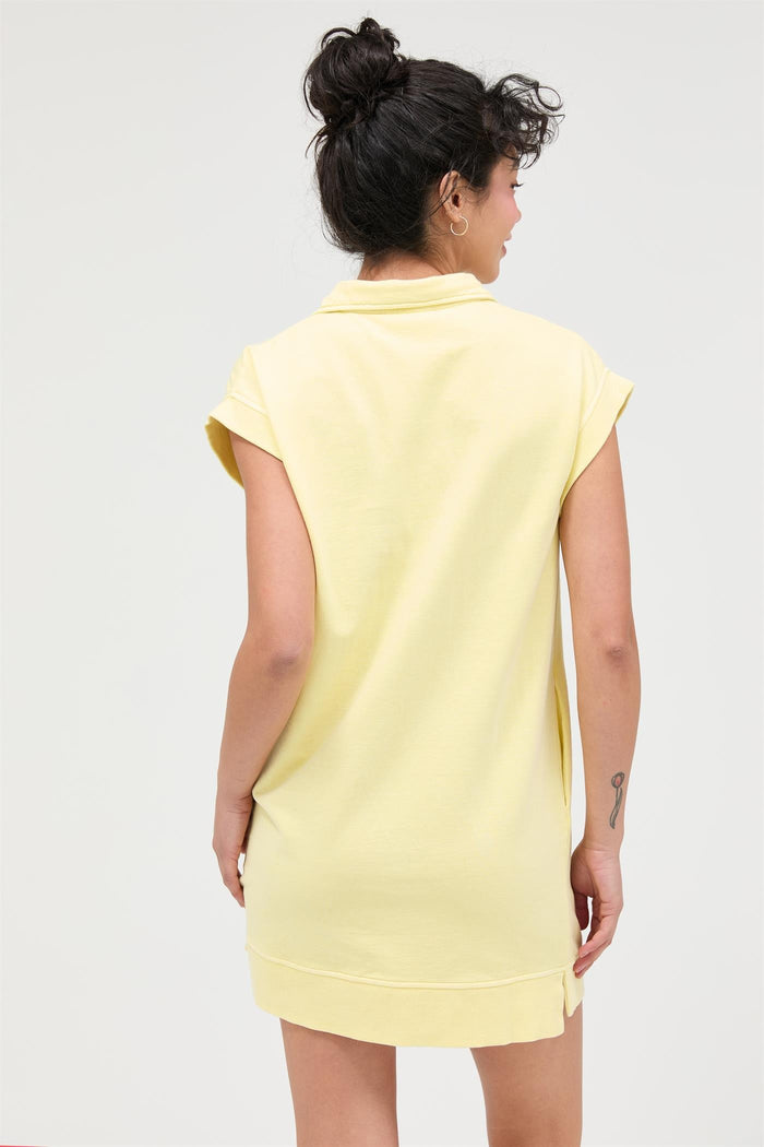 woman wearing a yellow short sleeve sweatshirt dress, seen from the back, with a relaxed fit and rolled sleeves