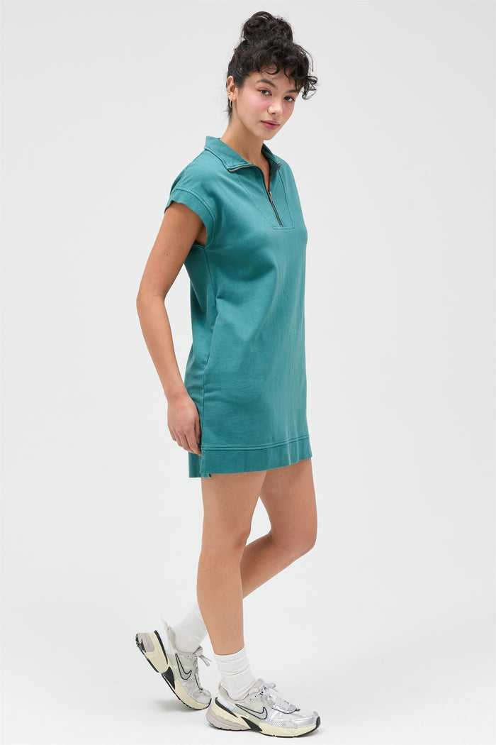 woman wearing a teal polo dress with a zipper collar and rolled sleeves, styled with sneakers