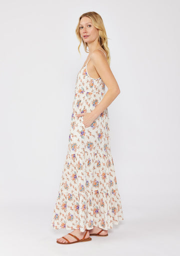 woman wearing a white floral maxi dress with thin straps and pockets, standing sideways with a light breeze in her hair