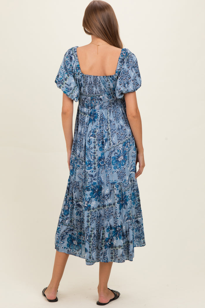 woman wearing a blue floral maternity maxi dress with puff sleeves and a smocked bodice, showing her baby bump from the back