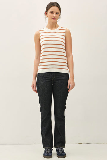 woman wearing a cream and orange striped sleeveless sweater with dark wash flared jeans and navy sneakers
