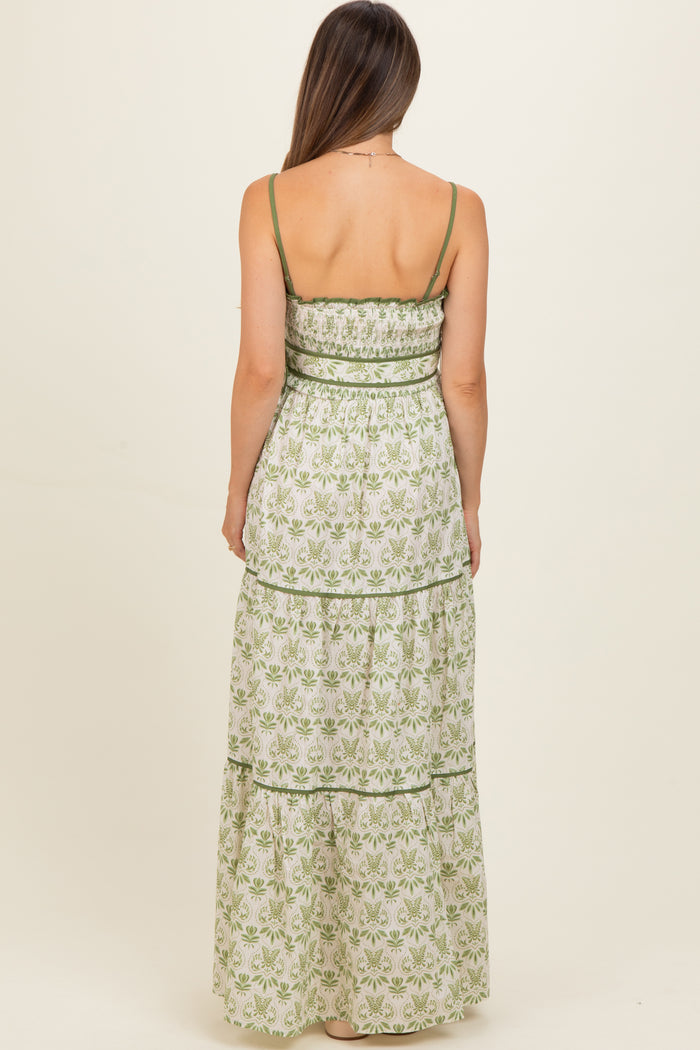 woman wearing a green and white floral maternity maxi dress with a tiered design and spaghetti straps