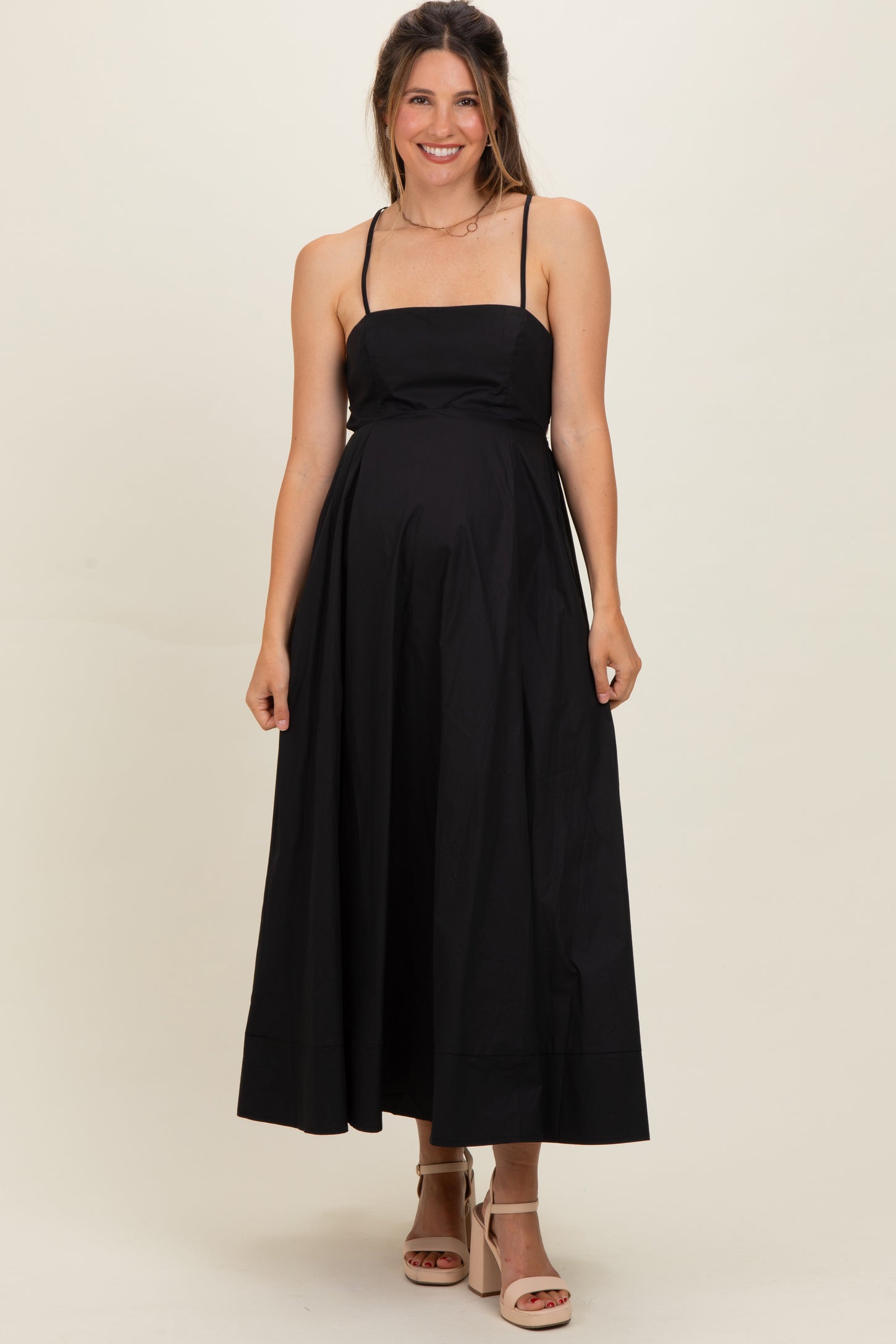 woman wearing a black maternity maxi dress with thin straps and a fitted bodice, showing her baby bump