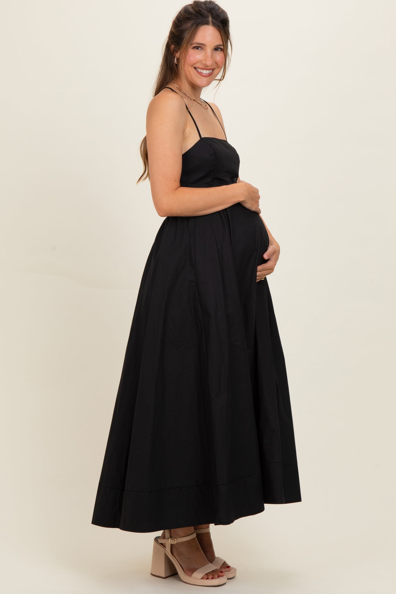 woman wearing a black maternity maxi dress with spaghetti straps and holding her baby bump