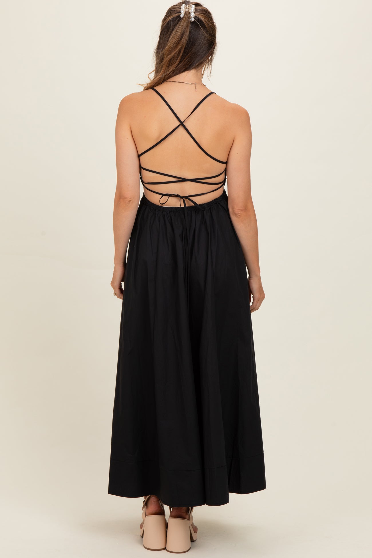 woman wearing a black maternity dress with a crisscross back and a flowy skirt, showing a baby bump