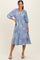 woman wearing a blue midi dress with floral print and balloon sleeves, standing in a relaxed pose