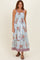 woman wearing a blue floral maxi dress with smocked bodice and patterned hem, posing with a natural expression