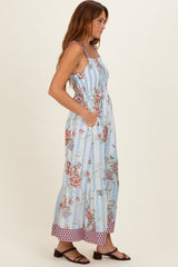 woman wearing a light blue floral maxi dress with smocked bodice and tiered skirt, standing sideways with pockets