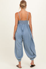 woman wearing a chambray maternity jumpsuit with a smocked bodice and loose, tapered legs